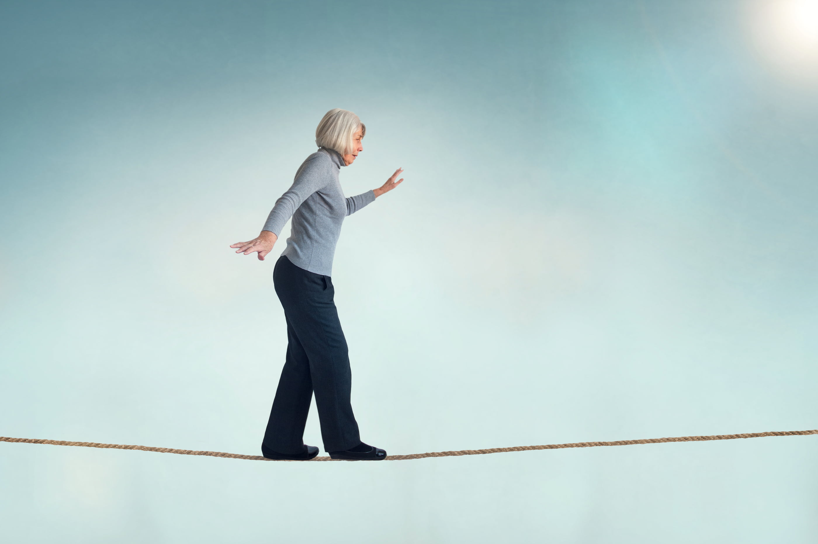 an older lady with white hair walking across a suspended rope