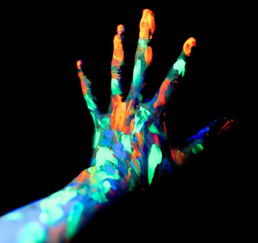 A pitch-black room and a hand covered in glowing neon paint